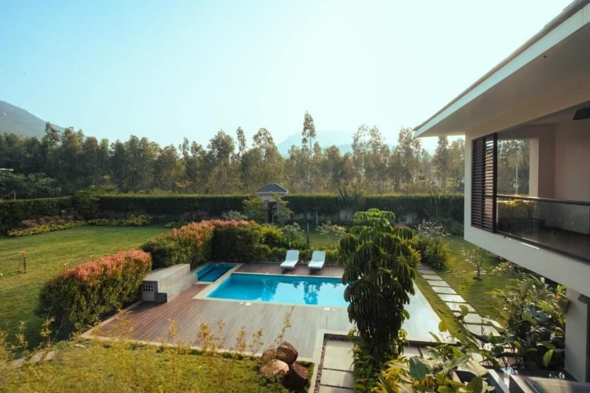 A modern outdoor pool area with two lounge chairs, surrounded by well-maintained landscaping and a view of a forested area.