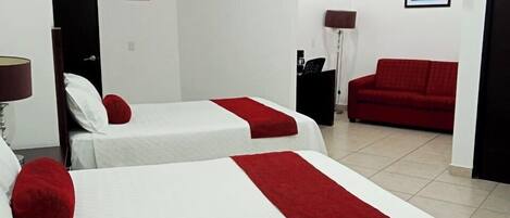Une chambre d’hôtel avec deux lits, un canapé rouge, un téléviseur fixé au mur et une porte avec un panneau indiquant la sortie.