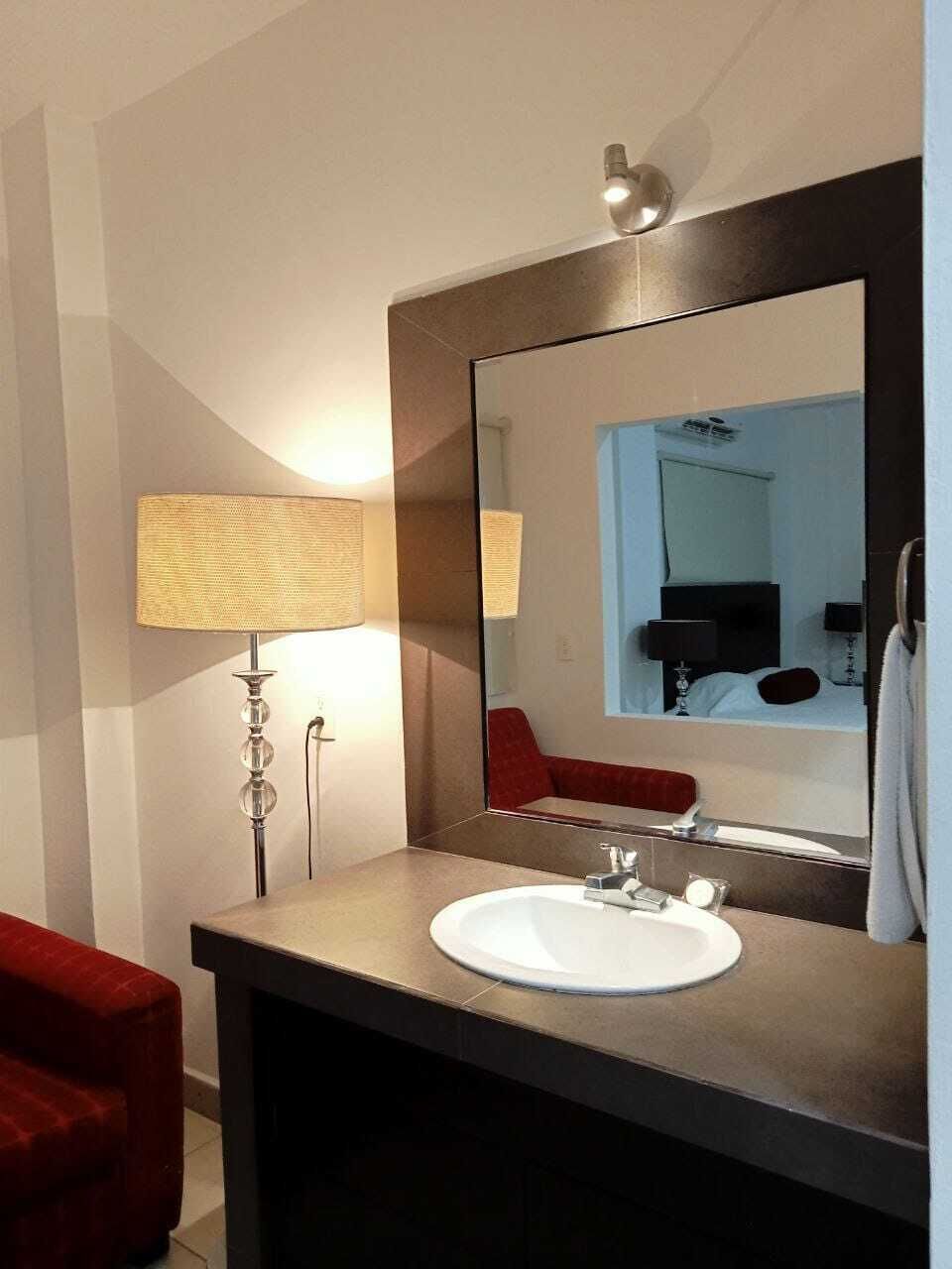 Un baño con un espejo grande, un lavabo redondo, una silla roja y una lámpara de pie.