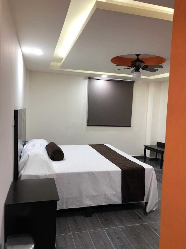 Habitación de hotel con cama, escritorio, ventilador de techo y una ventana grande.