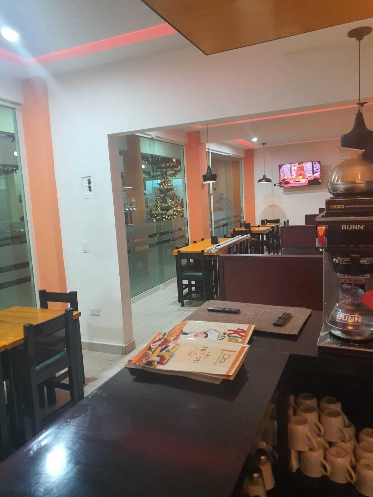 A restaurant with a Christmas tree, tables, chairs, and a Bunn water dispenser.