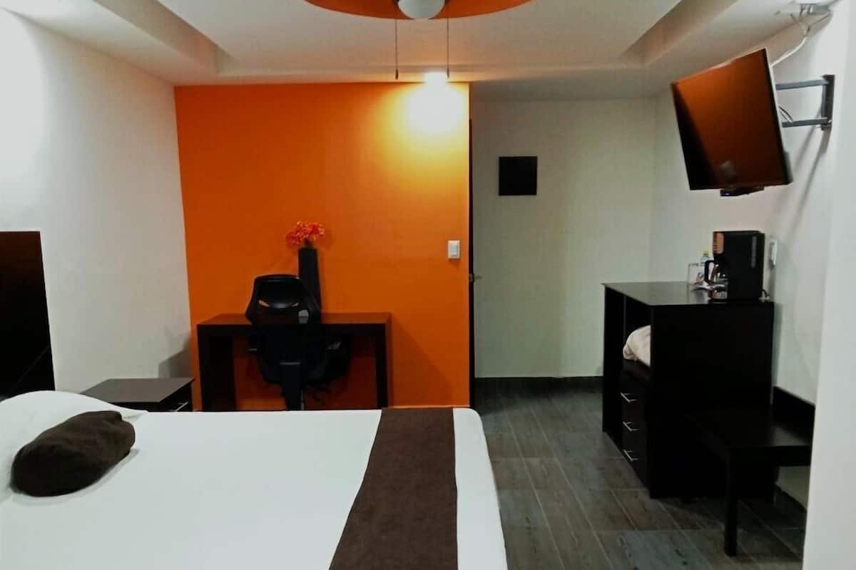 A hotel room with a bed, a desk, a chair, a TV, and a ceiling fan.