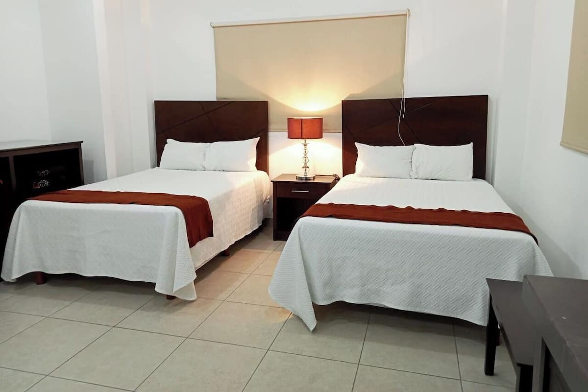 A hotel room with two single beds, a nightstand with a lamp, and a small table.