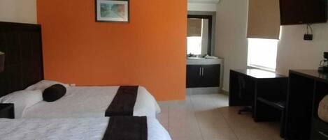 A hotel room with two beds, a desk, a chair, a television, and a window with blinds.