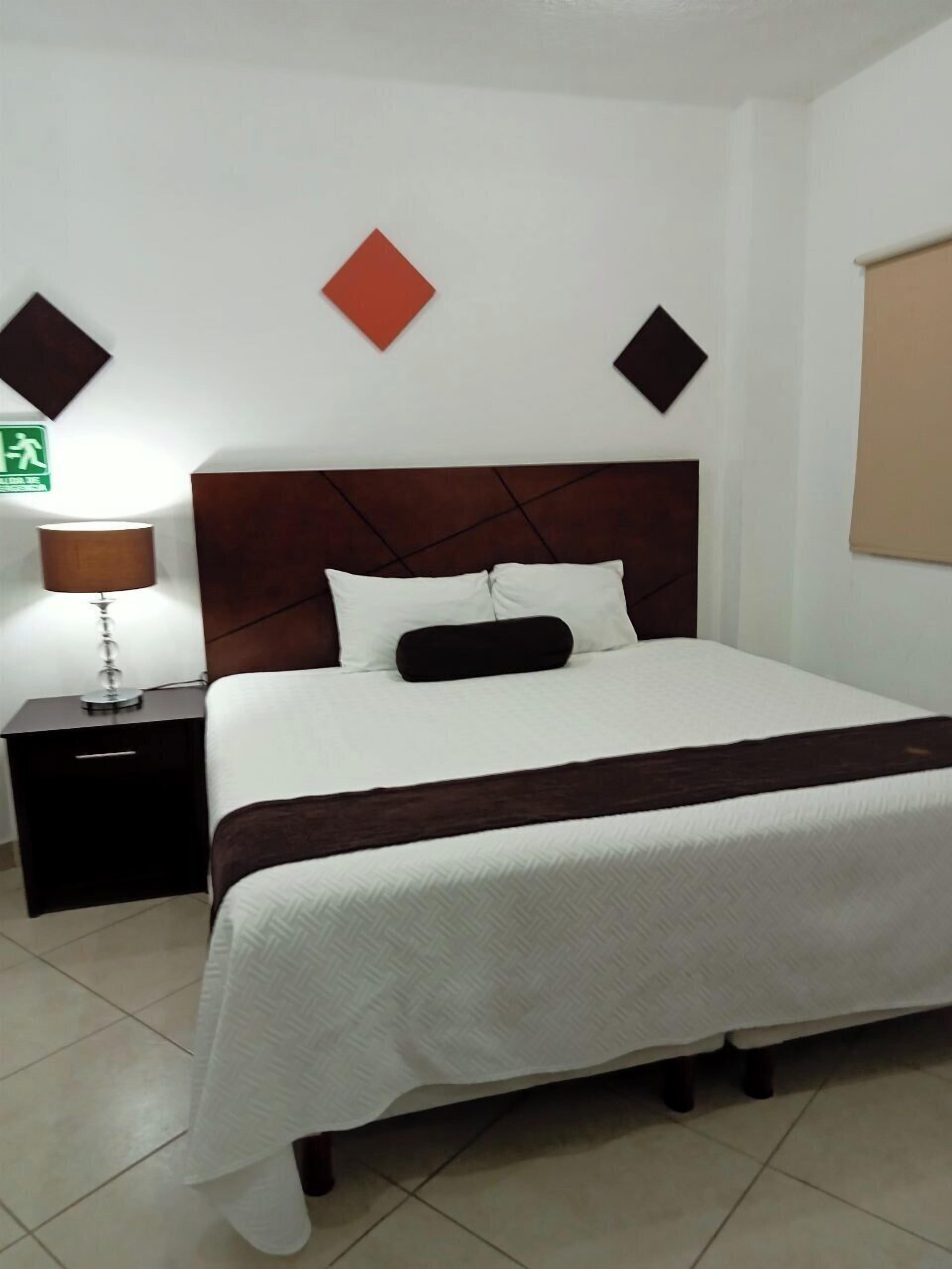 A neatly made bed with a white and brown bedspread, a wooden headboard, and a nightstand with a lamp.