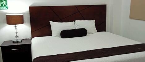 A neatly made bed with a white and brown bedspread, a wooden headboard, and a nightstand with a lamp.