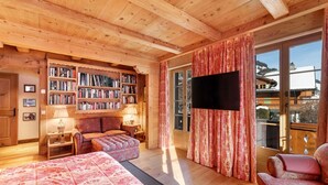 A cozy wooden cabin bedroom with a large bed, a bookshelf, a TV, and a view of the outside. - Beautiful Alpine Luxury Flat in Rougemont (Rougemont)