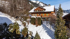 A wooden chalet with a snow-covered roof, surrounded by trees and a mountainous backdrop. - Beautiful Alpine Luxury Flat in Rougemont (Rougemont)