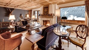 A cozy living room with a fireplace, wooden ceiling, and a view of a snowy forest. - Beautiful Alpine Luxury Flat in Rougemont (Rougemont)