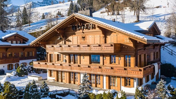 A large wooden chalet with multiple balconies, surrounded by snow-covered trees and a mountainous backdrop. - Beautiful Alpine Luxury Flat in Rougemont (Rougemont)