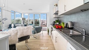 A modern kitchen with a stainless steel sink, a dining area with a white furry chair, and a view of the city through large windows. - Biscaya - Sauna, Shower, 360° Panoramic Rooftop Terrace, Floating House (Olpenitz)
