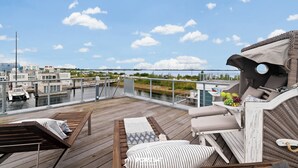 A deck with lounge chairs, a table with fruits, and a view of the marina and water. - Biscaya - Sauna, Shower, 360° Panoramic Rooftop Terrace, Floating House (Olpenitz)