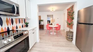 Une cuisine moderne dotée d’appareils électroménagers en acier inoxydable, un coin repas avec une table ronde et des chaises roses, et un parquet en bois clair.