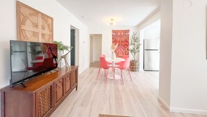 Un salon moderne doté d’un téléviseur à écran plat, d’un meuble en bois et d’un coin repas avec des chaises roses et une table blanche.
