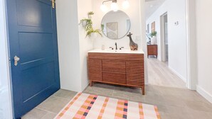 Une salle de bain avec une porte bleue, un meuble-lavabo en bois, un miroir rond et un tapis coloré.