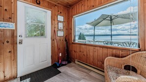 A wooden cabin with a white door, a large window with an umbrella, and a wicker sofa.