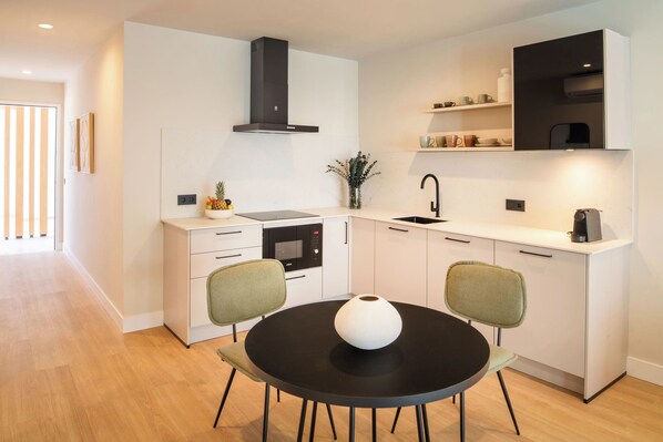 A modern kitchen with white cabinetry, a black stove, and a dining area with two chairs and a black table. - Vita Home Lanzarote I Deluxe Apartments (Arrecife)