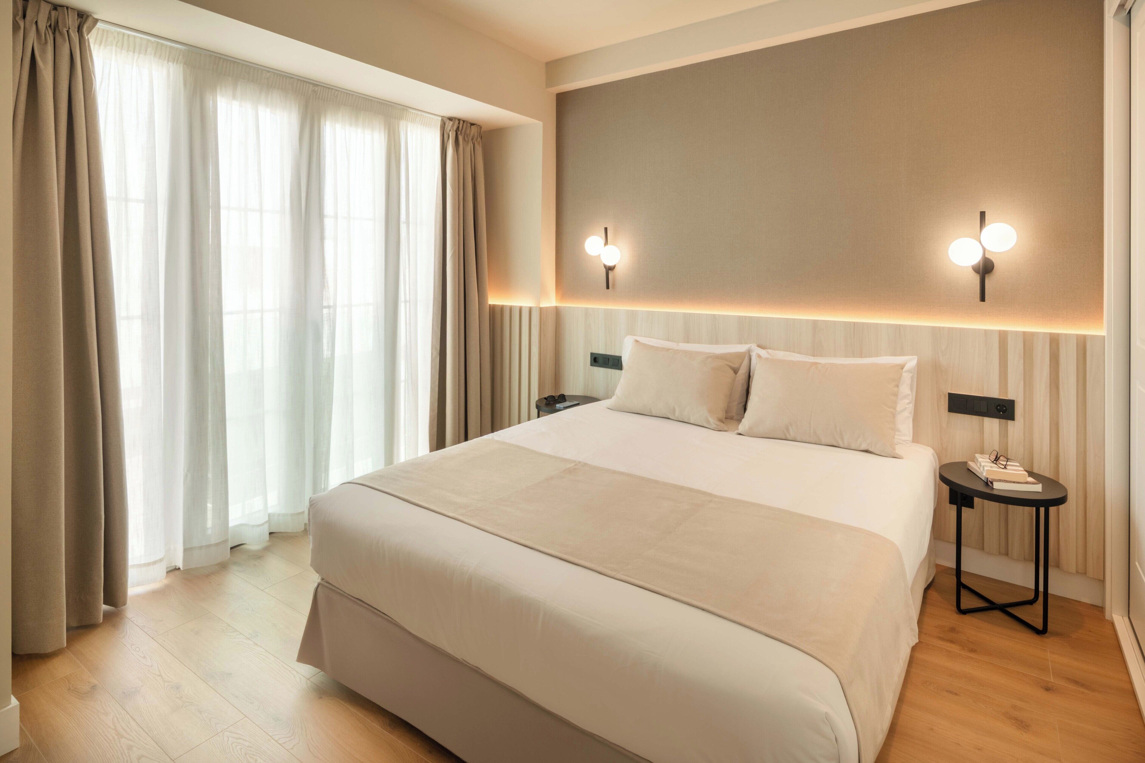 A hotel room with a large bed, two bedside tables, and a wall-mounted light fixture.