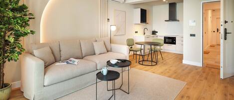A modern living room with a sofa, two small tables, a potted plant, and a kitchen in the background.