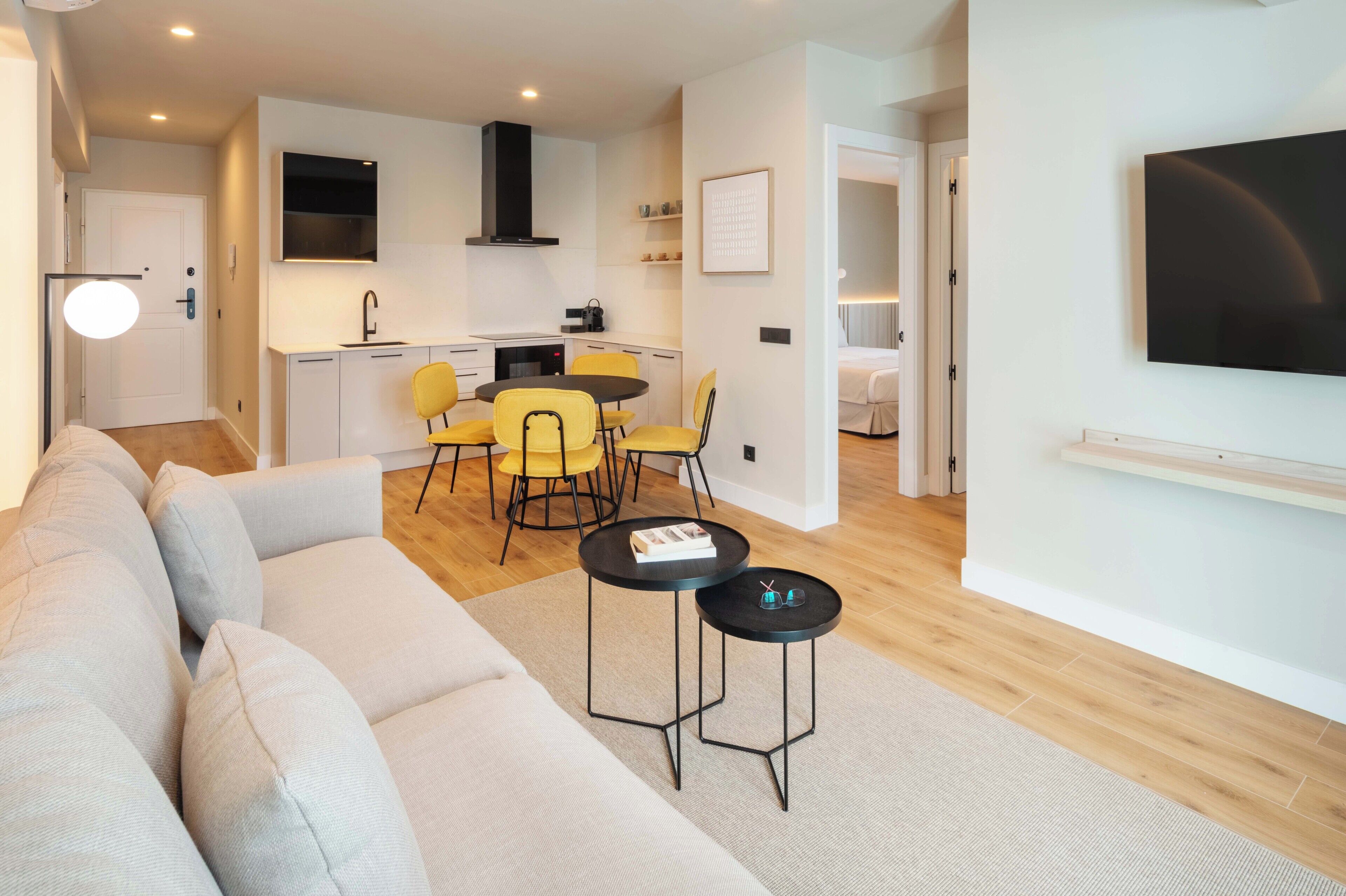 A modern living room with a sofa, two round tables, and a kitchen area with a dining table and chairs.