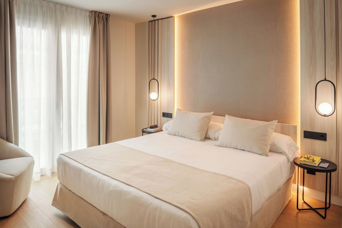 Habitació d'hotel moderna amb un llit gran, una taula de nit, una cadira i un taulell.