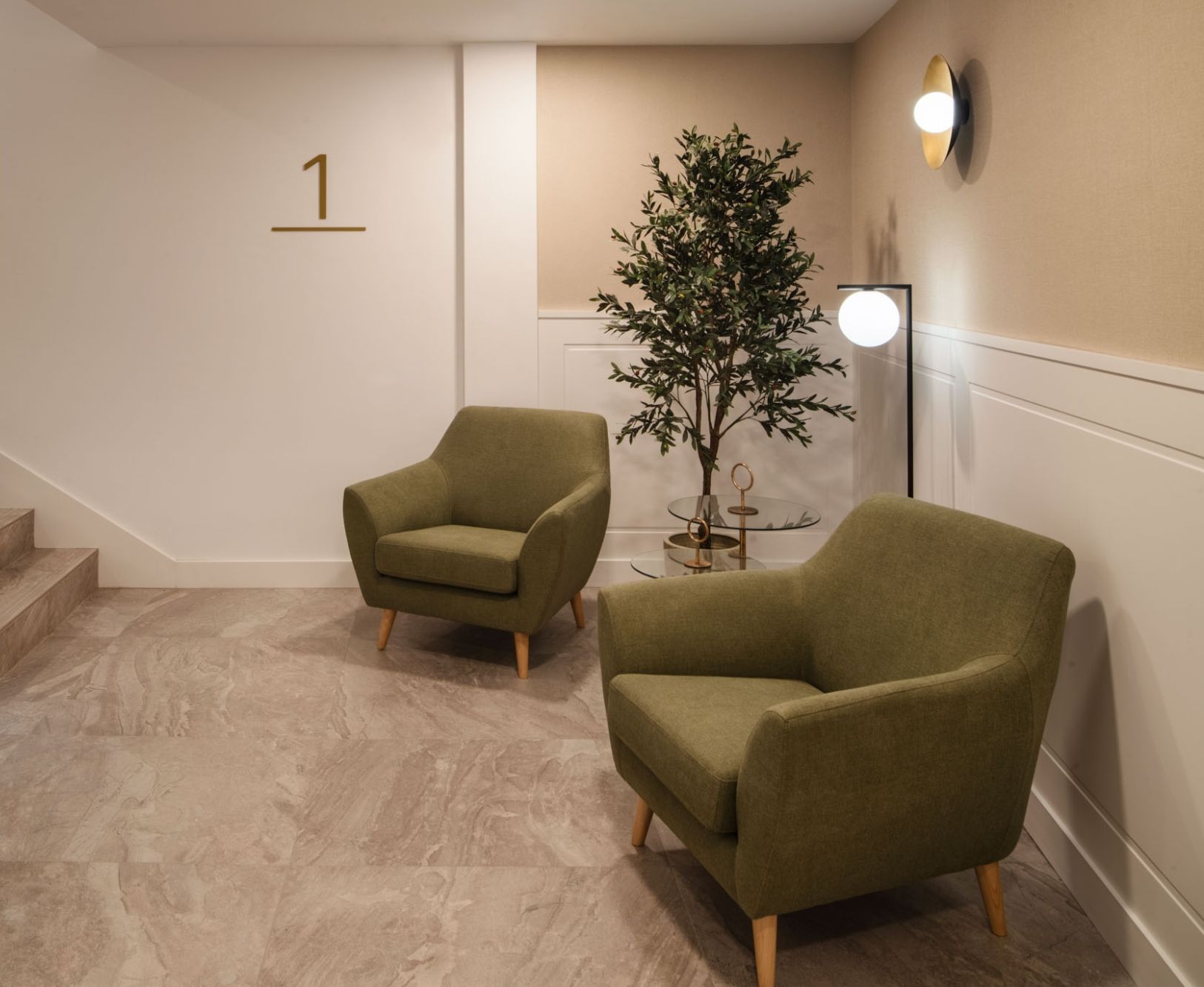 A modern interior with a staircase, two armchairs, a potted plant, and a wall-mounted light fixture.