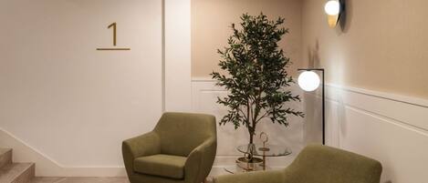A modern interior with a staircase, two armchairs, a potted plant, and a wall-mounted light fixture.