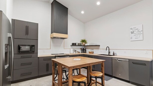 Una cocina moderna con armarios grises, una mesa de madera y dos taburetes.