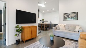 Una sala de estar moderna con un televisor de pantalla plana, un mueble de madera, un sofá gris y una mesa de centro redonda.