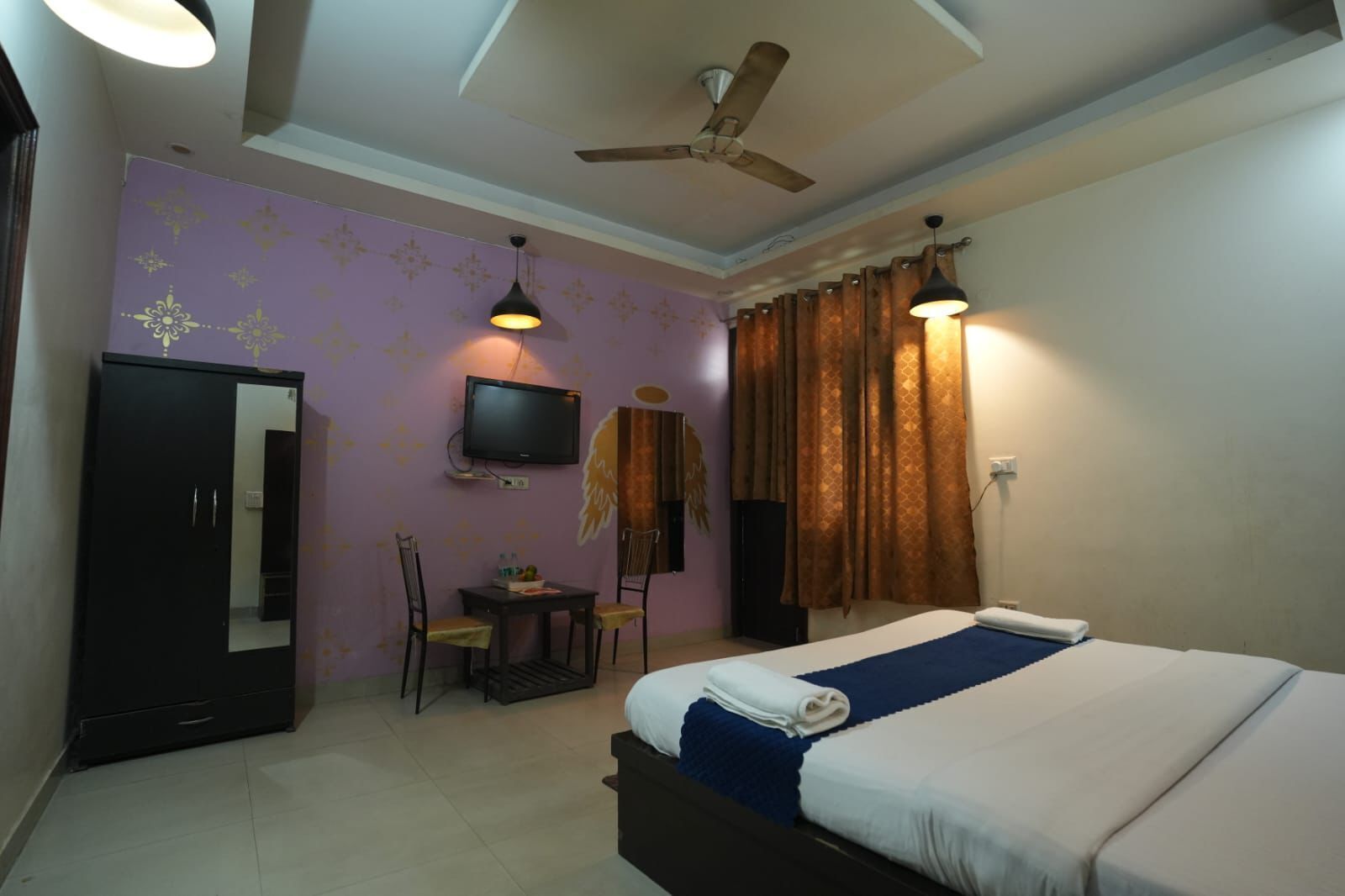 A hotel room with a bed, a desk with a chair, a television, and a ceiling fan.