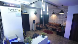 A hotel lobby with a reception desk, patterned sofas, hanging pendant lights, and a sign indicating airport taxi availability. - Hotel Kohinoor (New Delhi)