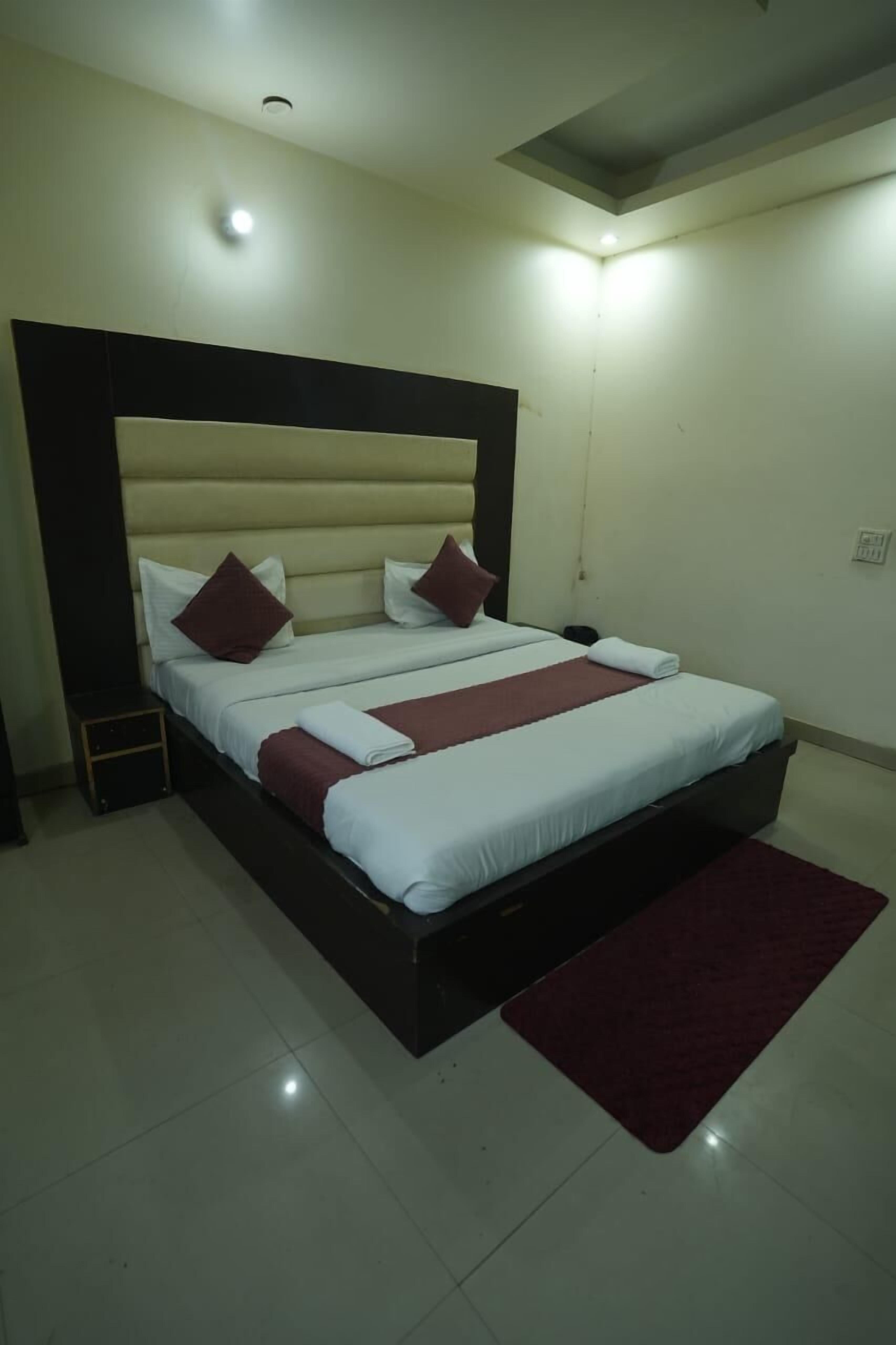 A double bed with a headboard, two pillows, a red throw blanket, and a matching red rug.
