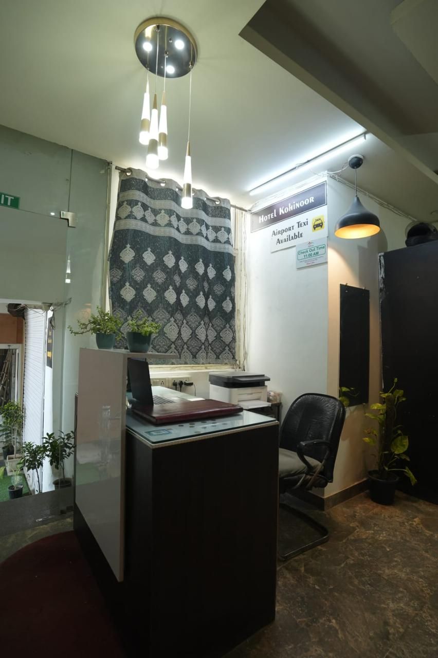 Un mostrador de recepción con una cortina estampada, un cartel que indica Hotel Kohinoor, y una lámpara en el techo.