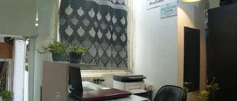 Un mostrador de recepción con una cortina estampada, un cartel que indica Hotel Kohinoor, y una lámpara en el techo.