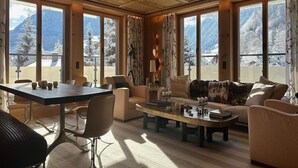 Een ruime woonkamer met een grote tafel, comfortabele zitplaatsen en uitzicht op met sneeuw bedekte bergen door grote ramen.