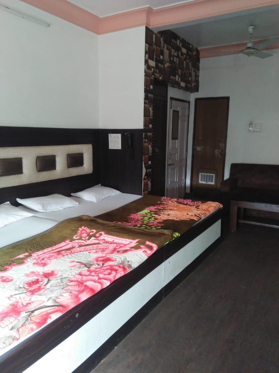 A single bed with a floral bedspread, a headboard with a white and black design, and a wooden door with a vent.