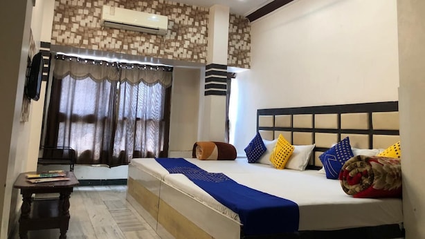 A bedroom with a bed, a desk, a chair, and a window with curtains. - Hotel Siddhartha (Ujjain)