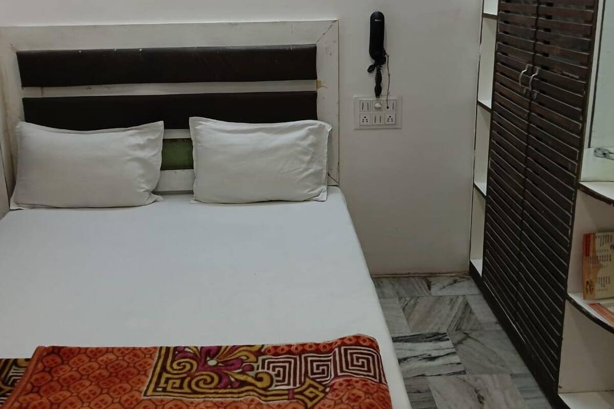 Ein kleiner, ordentlich eingerichteter Raum mit einem Bett, einem Telefon und einem Fenster mit Jalousien.