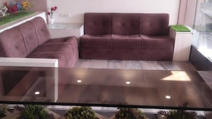 A reception area with a glass-top table, a sofa, and potted plants. - Hotel Siddhartha (Ujjain)