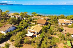 Μια παραθαλάσσια οικιστική περιοχή με σπίτια, μερικά από τα οποία έχουν κεραμοσκεπές, που περιβάλλεται από πράσινο και προσφέρει θέα στη θάλασσα.