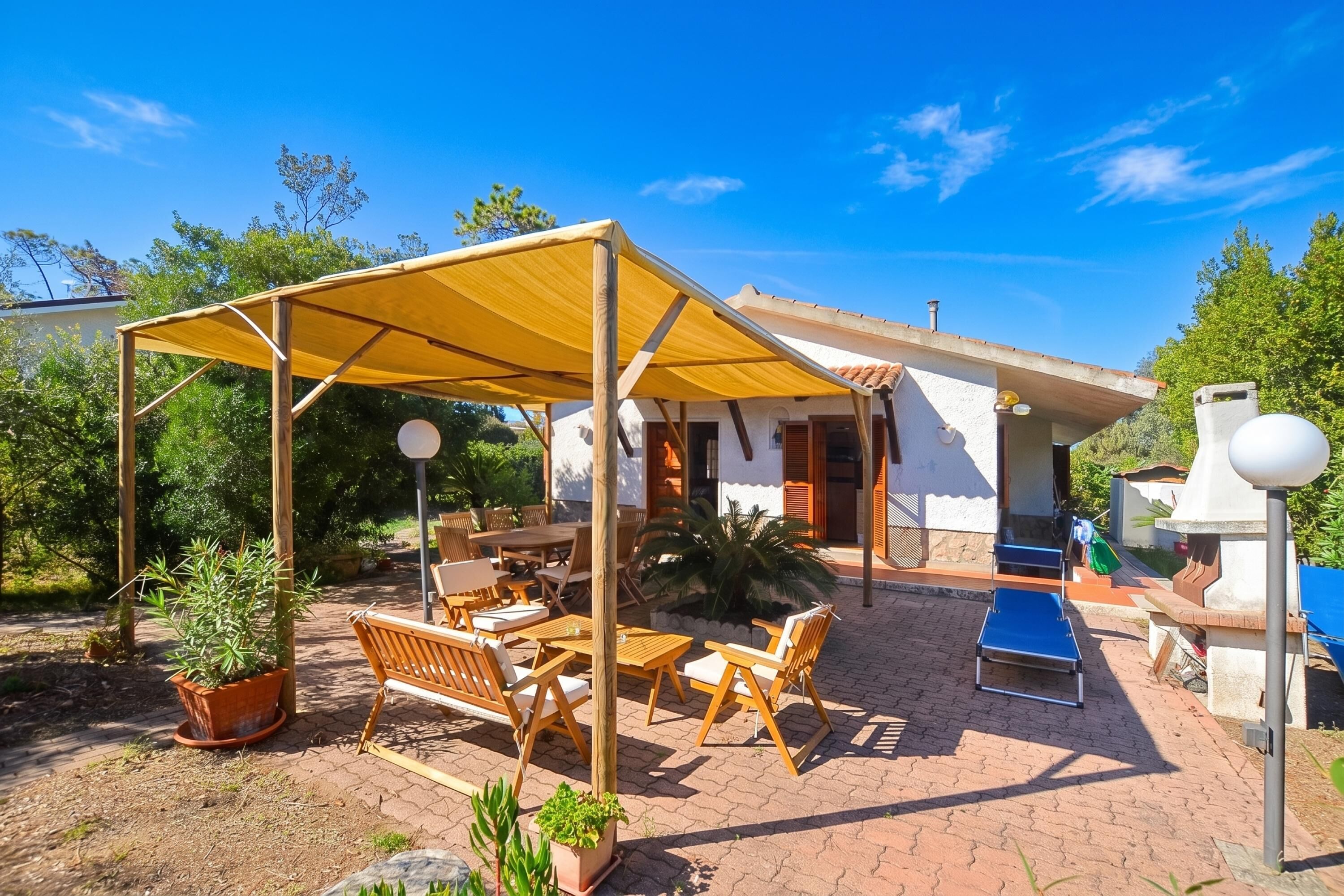 A covered outdoor seating area with wooden furniture, a barbecue grill, and a poolside lounge.