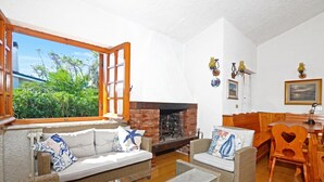 Un salon chaleureux, doté de meubles en osier, d’une cheminée et d’une grande fenêtre donnant sur un paysage verdoyant.