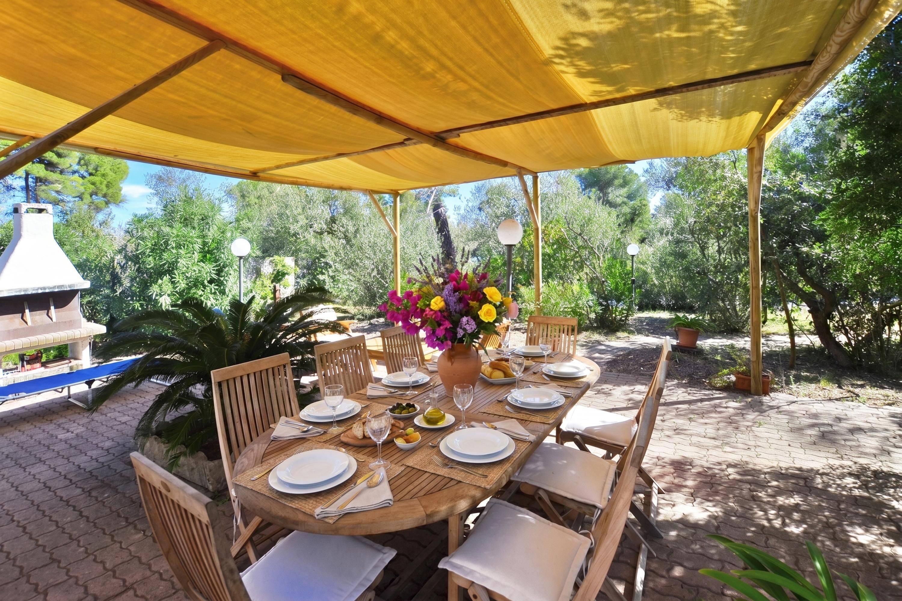 An outdoor dining area with a covered table, chairs, and a potted plant.