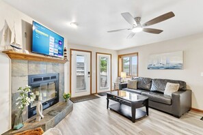 A living room with a fireplace, a flat-screen TV, a leather sofa, and a ceiling fan. - Ground Floor at Lighthouse Cove (Wisconsin Dells)