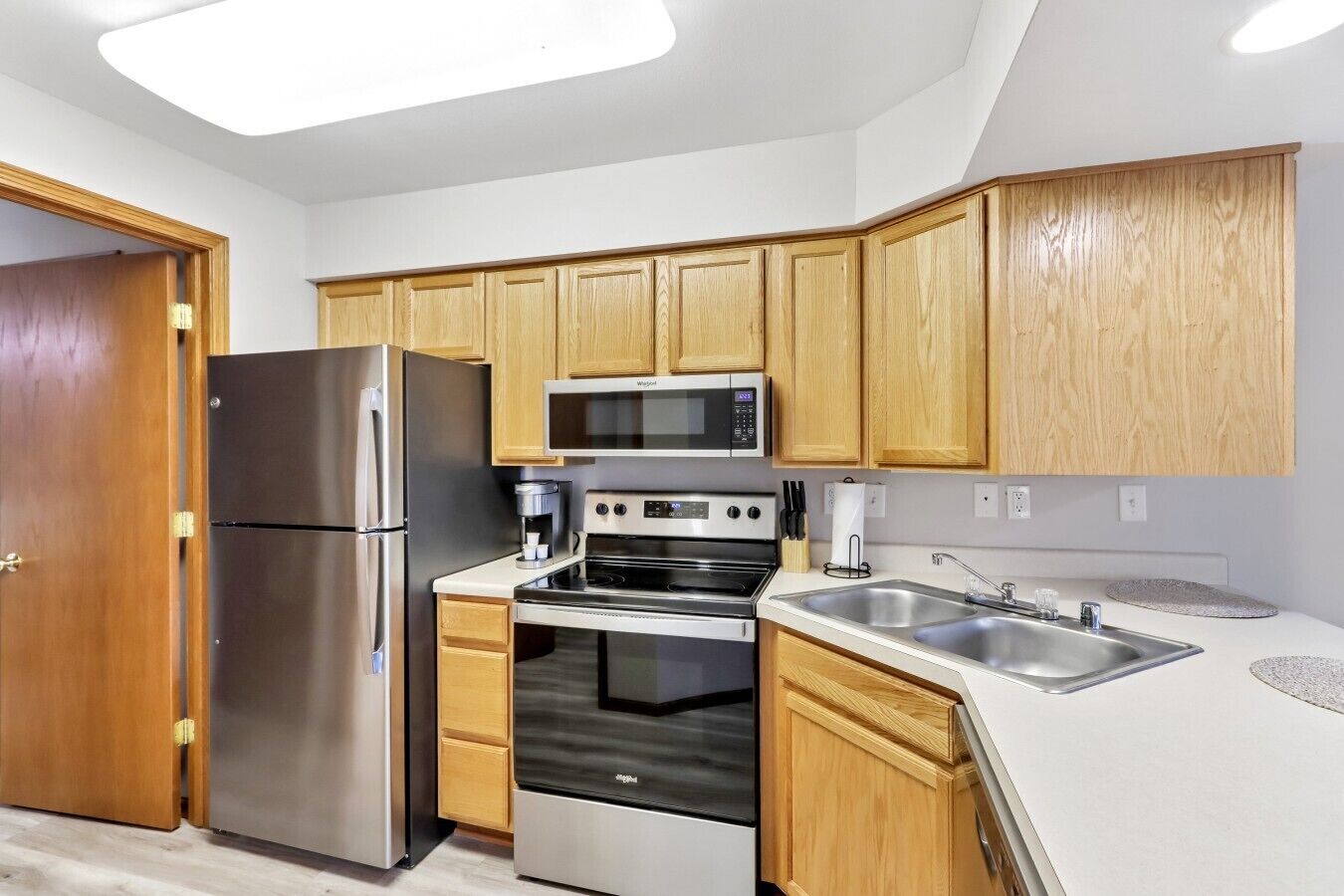 A modern kitchen with stainless steel appliances, wooden cabinets, and a white countertop.