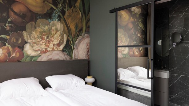 A hotel room with a bed, a nightstand, a mirror, and a large floral mural on the wall. - THE FRITZ HOTEL Amsterdam (Amsterdam)