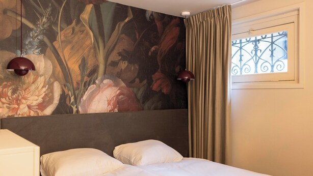 A hotel room with a bed, two lamps, a window with curtains, and a floral mural on the wall. - THE FRITZ HOTEL Amsterdam (Amsterdam)