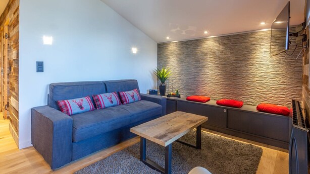Un salon moderne avec un canapé gris, une table basse en bois et un mur décoratif en pierre.