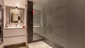 Une salle de bain moderne dotée d’une douche à parois de verre, d’un grand miroir et d’un lave-linge encastré.