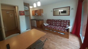 Een compacte woonruimte met een kitchenette, een bank, een eettafel en een spiegel.